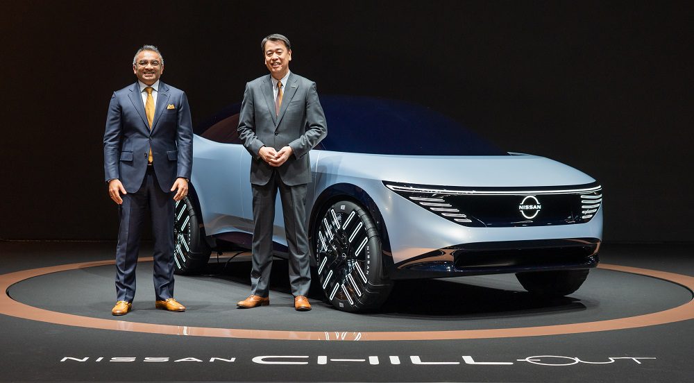 two men standing in front of a silver Nissan futuristic concept car
