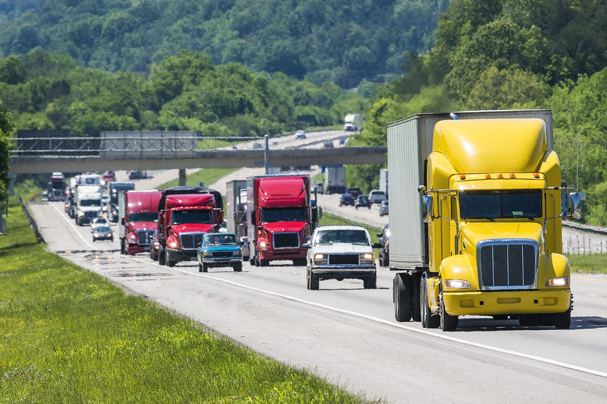 A yellow semi leads a packed line of traffic down an interstate