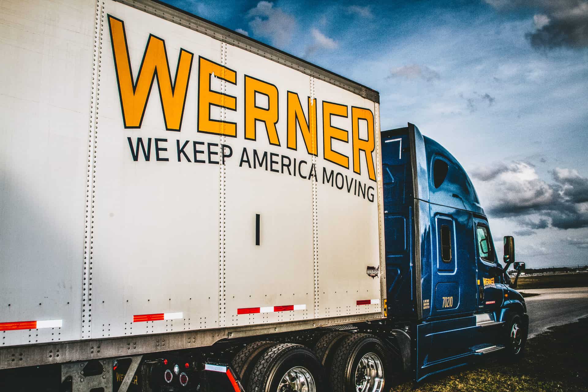 blue semi truck with white trailer with yellow words