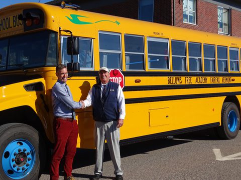 Representative from Anderson Motors with principal from Bellows Free Academy in front of an electric school bus